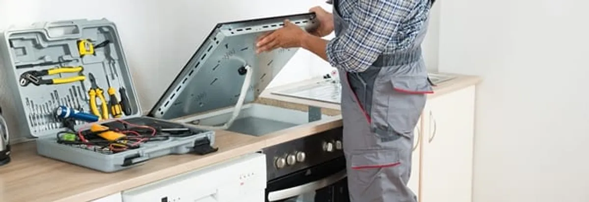 Cooktop repair technician lifting a built-in stovetop for service in Anchorage, AK