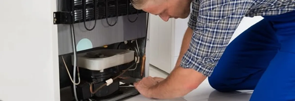 Refrigerator repair technician servicing the compressor and condenser area in Anchorage, AK