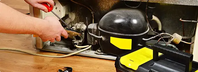 Refrigerator repair technician fixing the compressor and wiring in Anchorage, AK